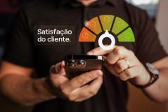 Mãos segurando um celular sob uma caixa com o texto 