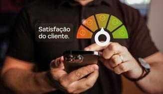 Mãos segurando um celular sob uma caixa com o texto 