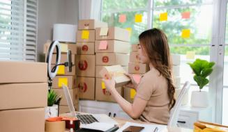 Mulher organizando caixas de embalagem para envio em um escritório bem iluminado, ideal para negócios de comércio eletrônico e logística.